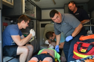 Three students and instructor in an ambulance learning paramedic techniques on a medical dummy.