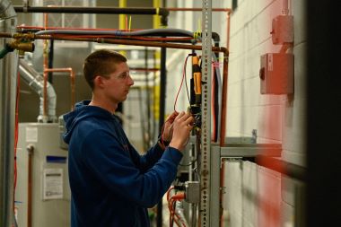 An air conditioning student examining an electrical output.
