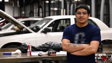 Automotive student posing for candid shot with a car in the background