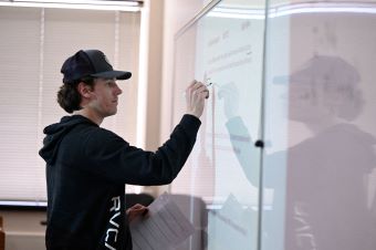 A math student writing out an equation on the board.