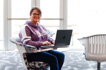 A student sitting in the lounging area with her laptop in the library. 