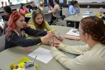 Three early childhood education students creating a structure out of plastic material.