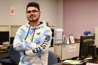 A student worker standing next to his desk.