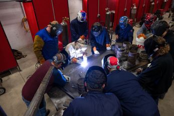 Welding students as a group watching over materials being worked on. 