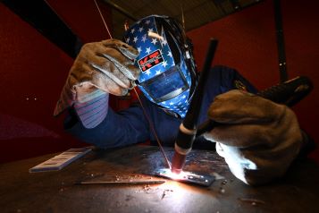 A welding student welding metal material together with a shield on. 